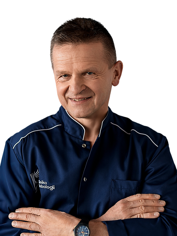 Portret dr. Jerzego Leszczyńskiego, chirurga naczyniowego z Kliniki Flebologii. Lekarz o krótkich, ciemnych włosach uśmiecha się łagodnie, mając skrzyżowane ramiona. Jest ubrany w granatowy uniform medyczny z białym logo kliniki na piersi. Zdjęcie na czystym, białym tle.