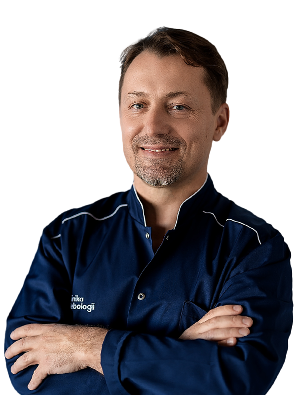 Portret dr. hab. n. med. Michała Zawadzkiego, radiologa interwencyjnego z Kliniki Flebologii. Uśmiechnięty lekarz z krótkim zarostem i ciemnymi włosami pozuje ze skrzyżowanymi ramionami. Ma na sobie granatowy uniform medyczny z logo kliniki. Zdjęcie na jasnym, białym tle.