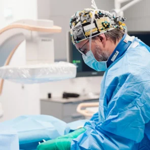 Radiolog flebolog - Cezary Szary - w sterylnym stroju i czepku chirurgicznym podczas zabiegu embolizacji żylnej w nowoczesnej pracowni zabiegowej procedur interwencyjnych - Klinika Flebologii Warszawa.